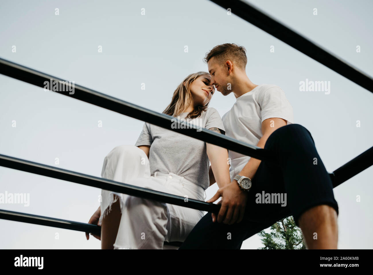 Joven pareja besándose mutuamente en un marco de escalada Foto de stock