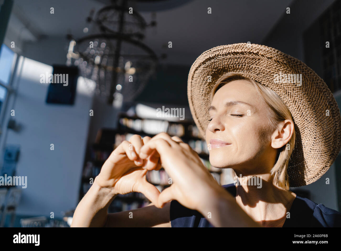 Mujer con sombrero de paja, mirando hacia el sol, haciendo dedo en forma de corazón frame Foto de stock