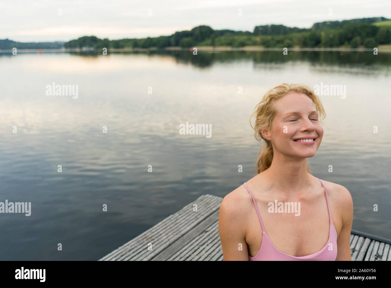 Mujer sonriente con los ojos cerrados en un muelle en un lago Foto de stock