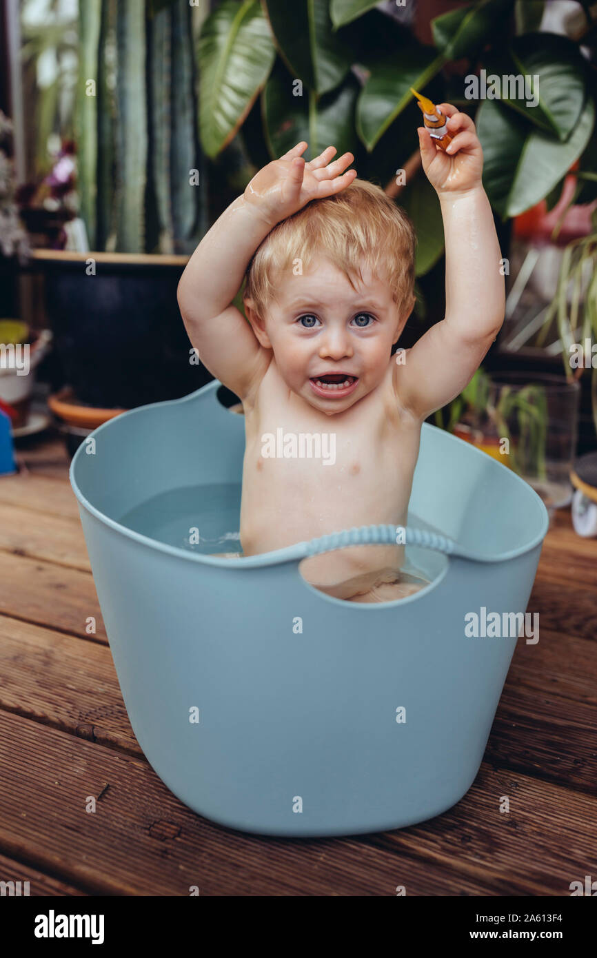 Baby Boy sentado en el baño del bebé en el balcón, jugando con un juguete Foto de stock