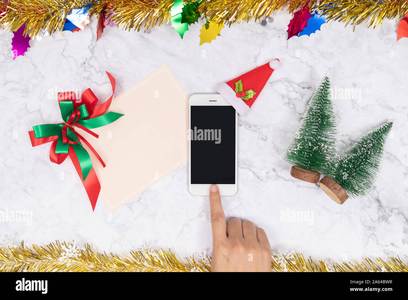 Las compras online en regalos de temporada durante las vacaciones de Navidad. Mujer toque el botón de teléfono móvil decorar con felpa de terciopelo rojo gorro de Papá Noel con puños, blanco Foto de stock