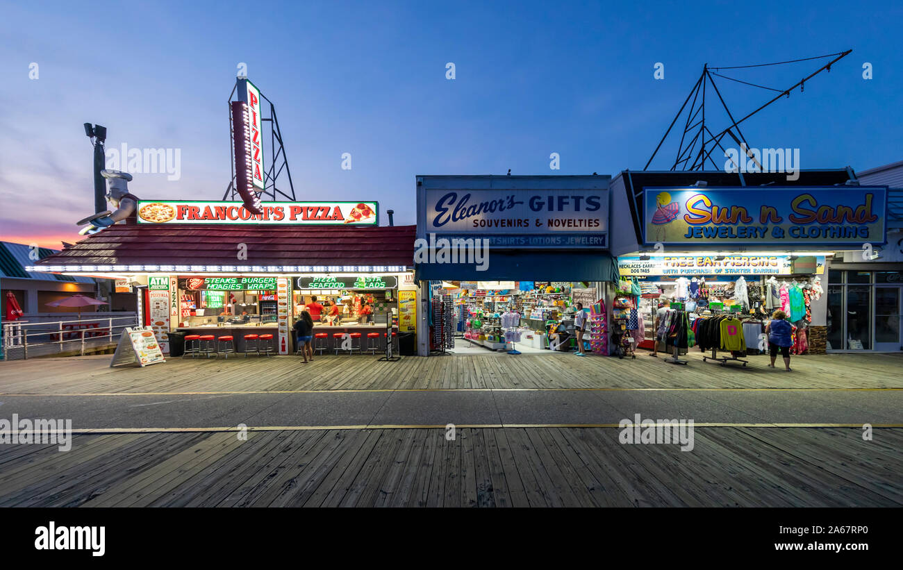 Un pequeño número de personas a pie y visitar tiendas y salas de juegos en un paseo marítimo de madera casi vacía en la noche cuando el verano ha terminado. Foto de stock