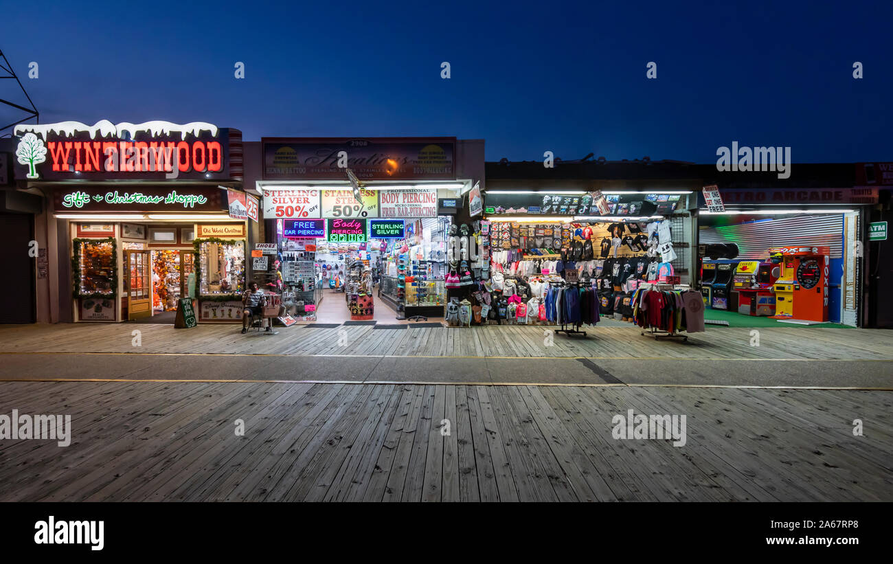 Un pequeño número de personas a pie y visitar tiendas y salas de juegos en un paseo marítimo de madera casi vacía en la noche cuando el verano ha terminado. Foto de stock