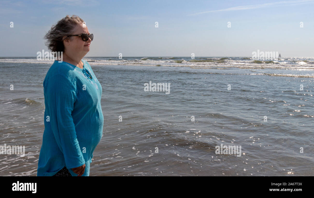 Una mujer mayor disfrutando de caminar en la arena de la playa por la orilla del océano. Foto de stock
