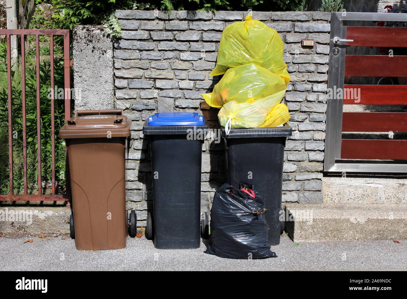 Tres diferentes contenedores de basura de plástico para la ordenación  ecológica para el reciclado de basura con bolsas de plástico en la parte  frontal de la casa de la familia piedra y