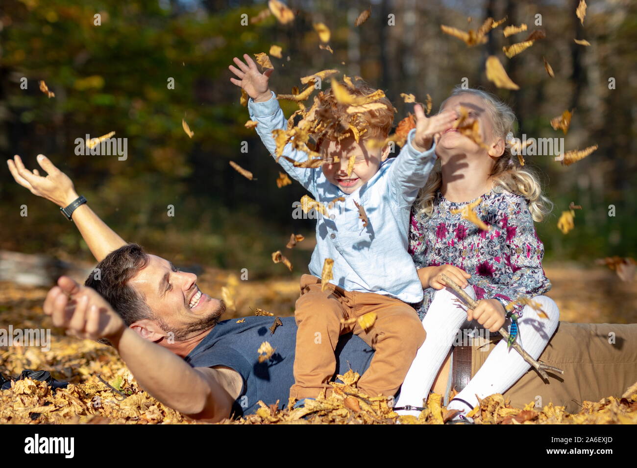 Feliz papá y niños jugando con las hojas de otoño en el bosque Foto de stock