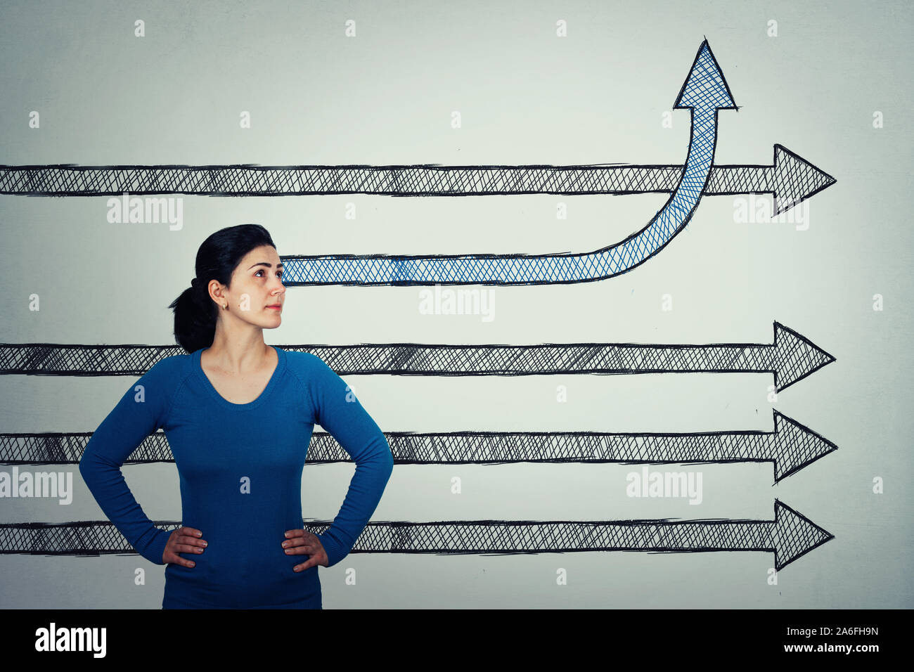 Mujer decidida, las manos en las caderas, mirando hacia arriba como la flecha straigth bocetos van por delante y uno cambia de dirección doblado hacia arriba. Concepto diferentes de pensamiento, bre Foto de stock