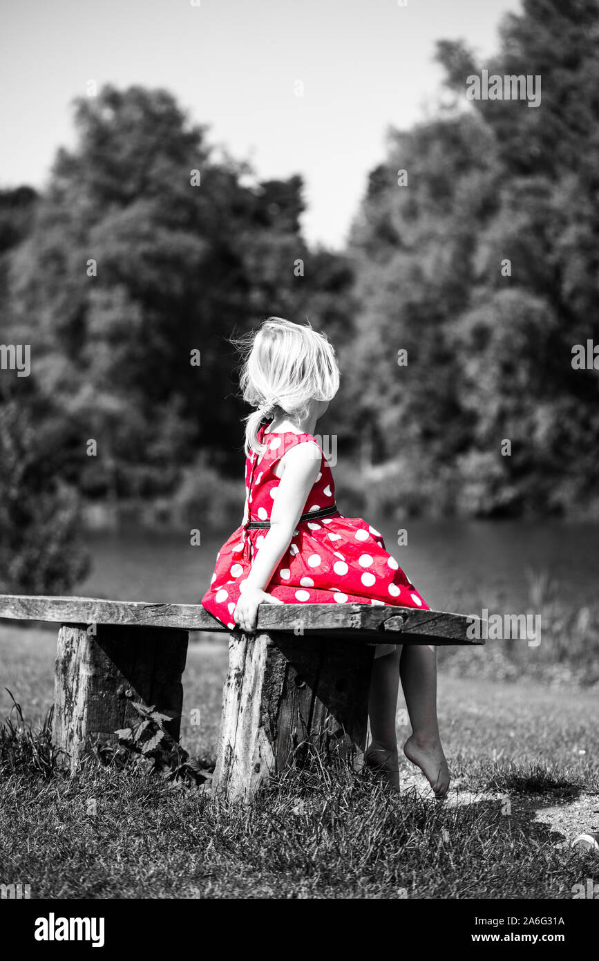 Una niña en un bonito vestido rojo, sentado en un banco solo, Color, Color pop  pop Fotografía de stock - Alamy