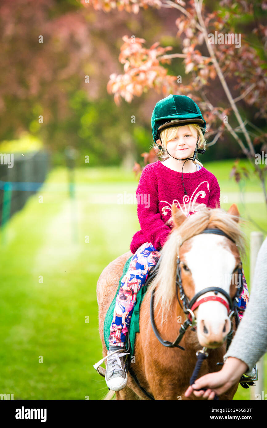 Una bonita niña lindo tomar una lección de equitación con un instructor, vistiendo un sombrero de montar a caballo en los jardines Trentham, Stoke on Trent Foto de stock