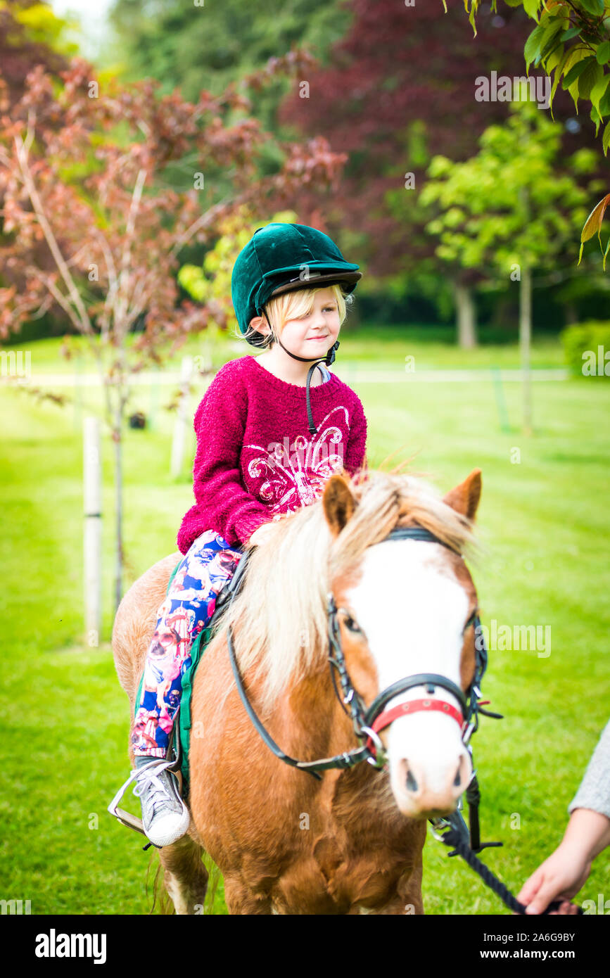 Una bonita niña lindo tomar una lección de equitación con un instructor, vistiendo un sombrero de montar a caballo en los jardines Trentham, Stoke on Trent Foto de stock