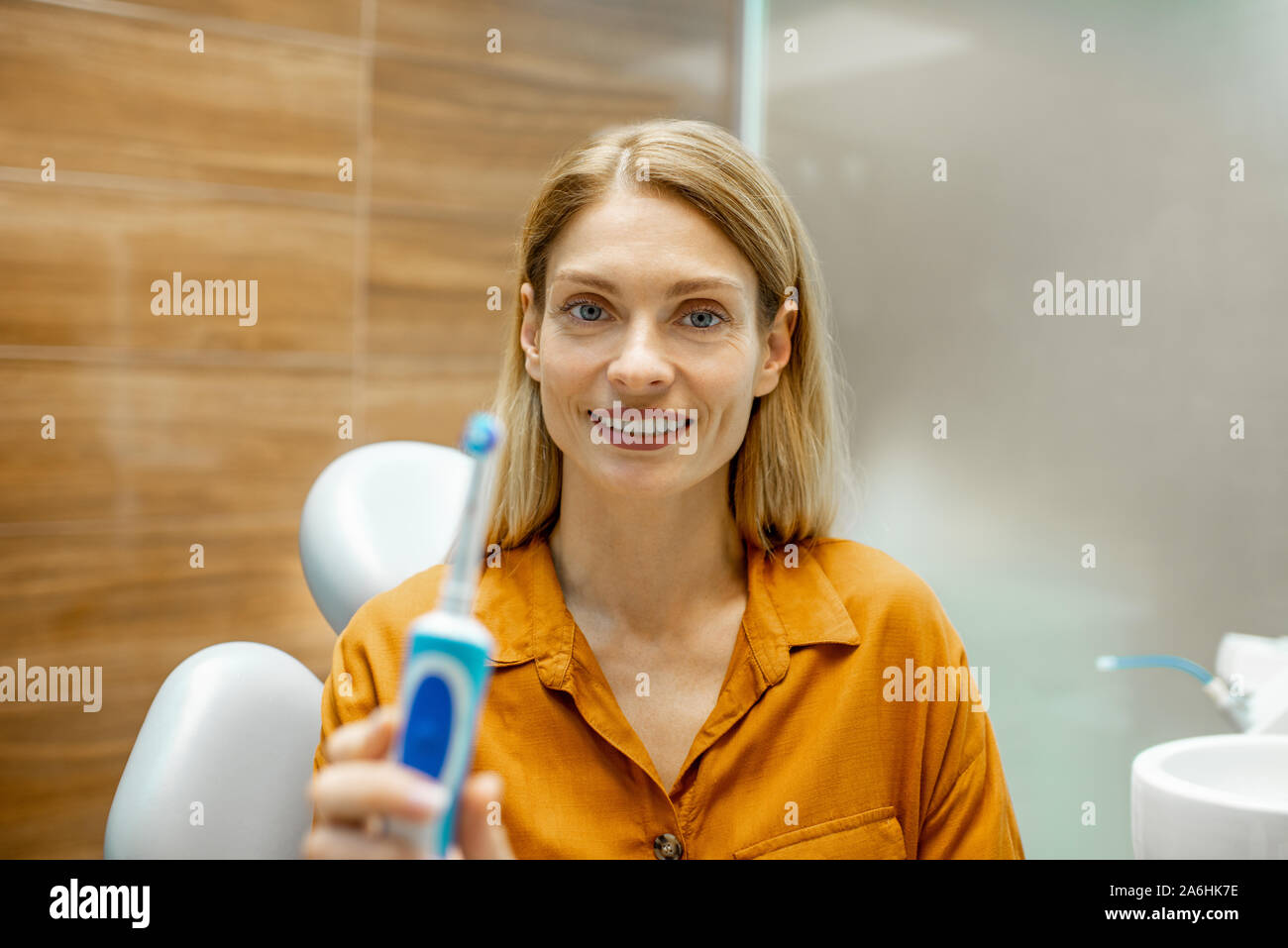 Retrato de una mujer hermosa y alegre como un cepillo de dientes eléctrico con el paciente sentado en el sillón dental en el consultorio dental Foto de stock