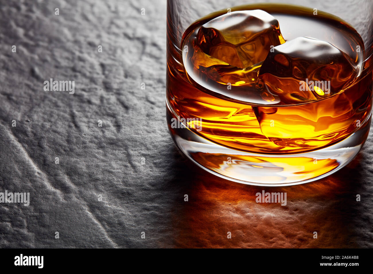 Elegante vaso de whisky con cubitos de hielo sobre la mesa de piedra negra. Moody Vista cercana Foto de stock