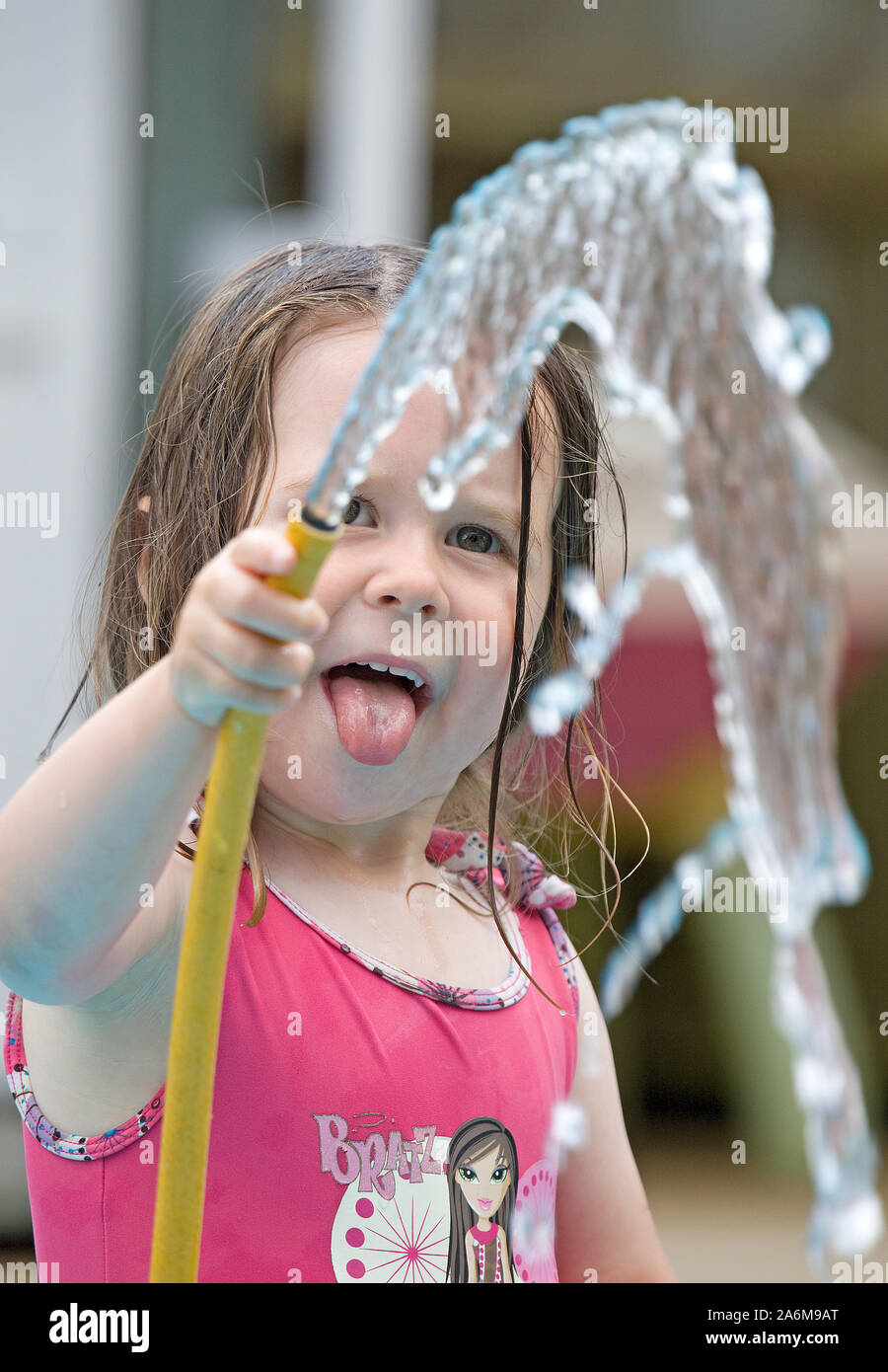Niña de 4 años de edad con la lengua fuera la celebración de manguera con agua fluyendo en el aire Foto de stock