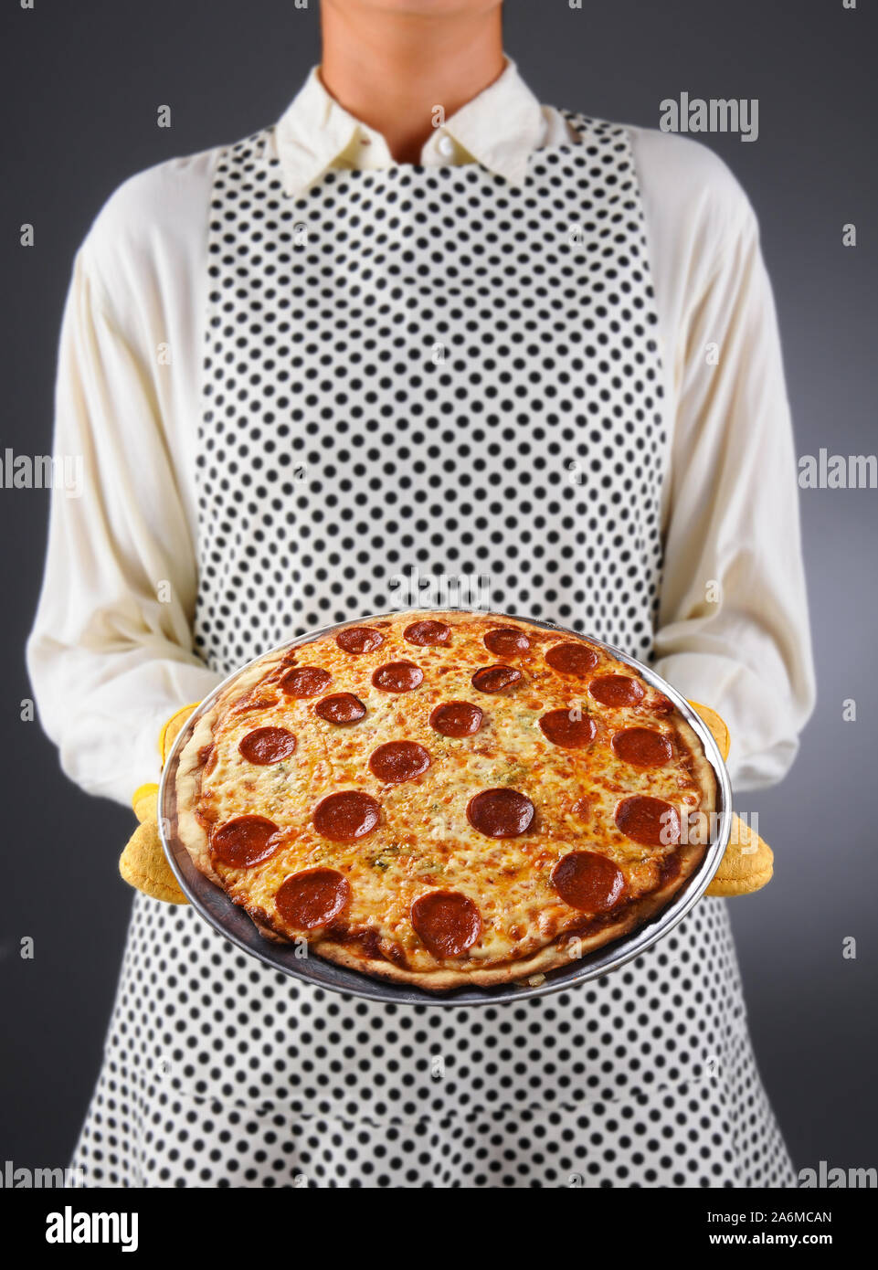 Primer plano de un ama de casa en un delantal y manoplas mantiene fresca pizza casera. La mujer es irreconocible. Foto de stock