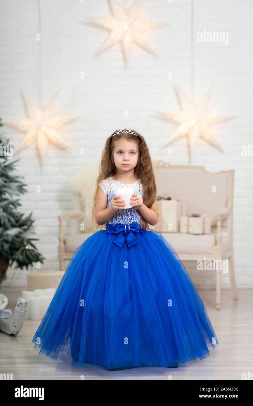 Cute little girl en un magnífico vestido azul sosteniendo una vela en sus  manos artificiales para la decoración del hogar en Navidad. Escena  infantiles Fotografía de stock - Alamy