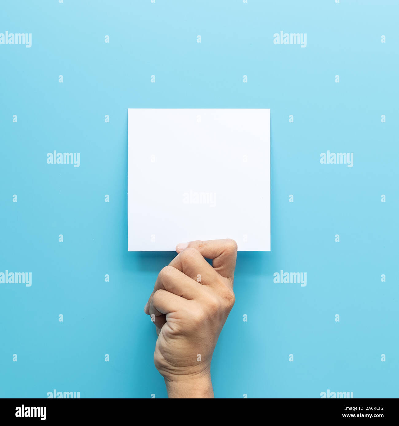 Hombre mano sujetando la tarjeta en blanco hoja de papel aislado sobre fondo azul con espacio de copia. Foto de stock