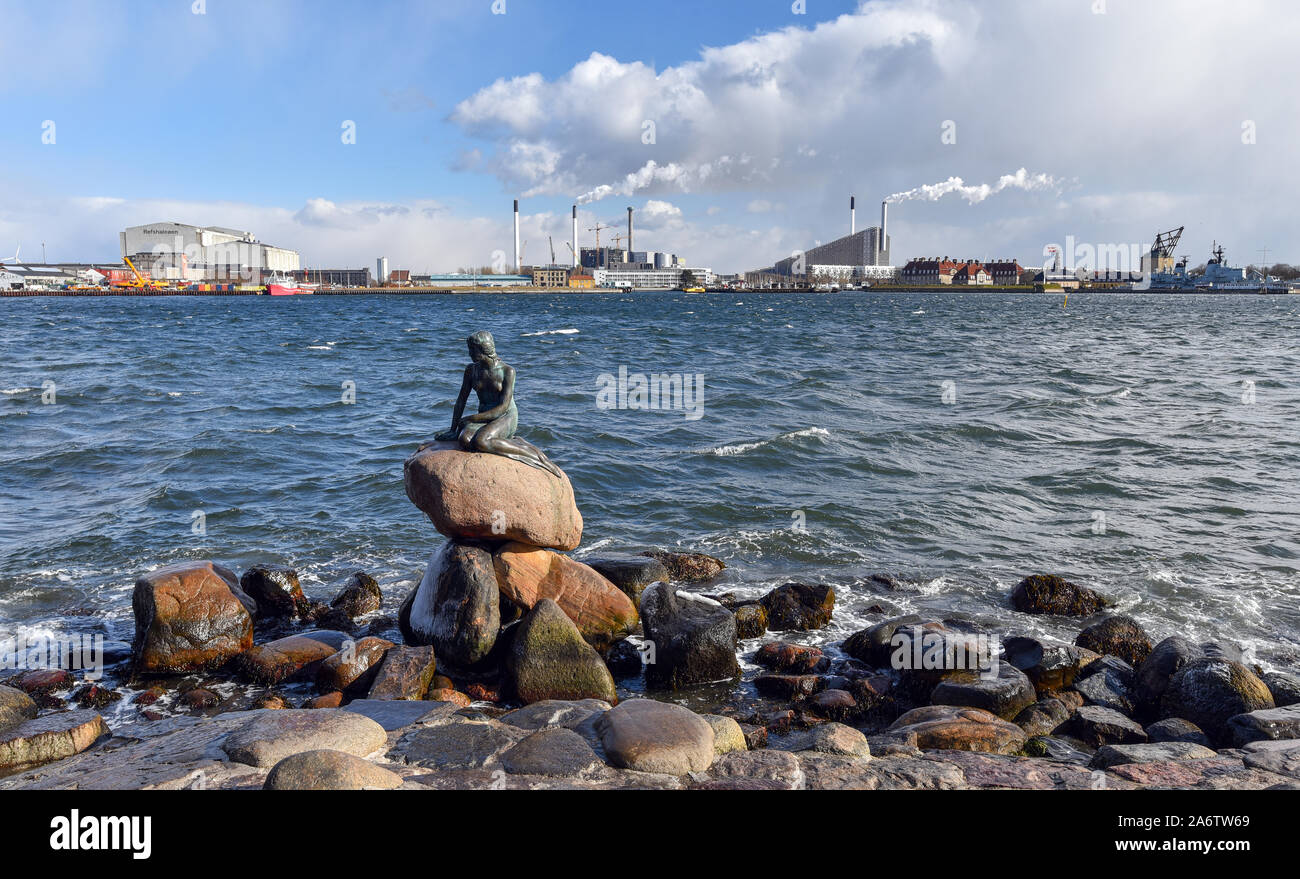 Copenhague, Dinamarca - 16 de marzo de 2018: la famosa Sirenita delante de fumar chimeneas de las fábricas en el fondo. Foto de stock