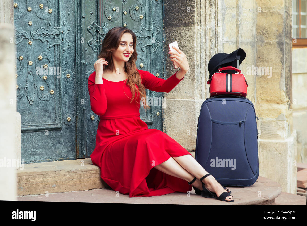 Hermosa mujer turística lleva vestido rojo con una maleta toma selfie por  smartphone mientras sentado en las escaleras de la calle de la ciudad  Fotografía de stock - Alamy