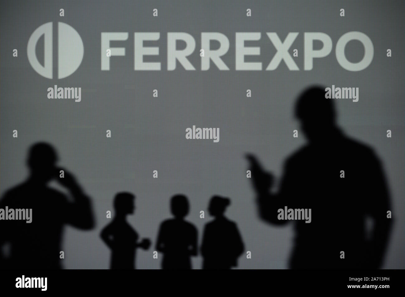 El logotipo de Ferrexpo es visto en una pantalla LED en el fondo mientras una silueta persona utiliza un smartphone (uso Editorial solamente) Foto de stock