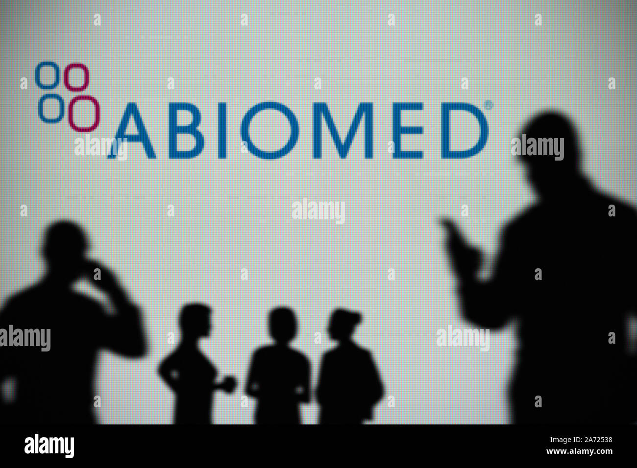El logotipo Abiomed es visto en una pantalla LED en el fondo mientras una silueta persona utiliza un smartphone (uso Editorial solamente) Foto de stock