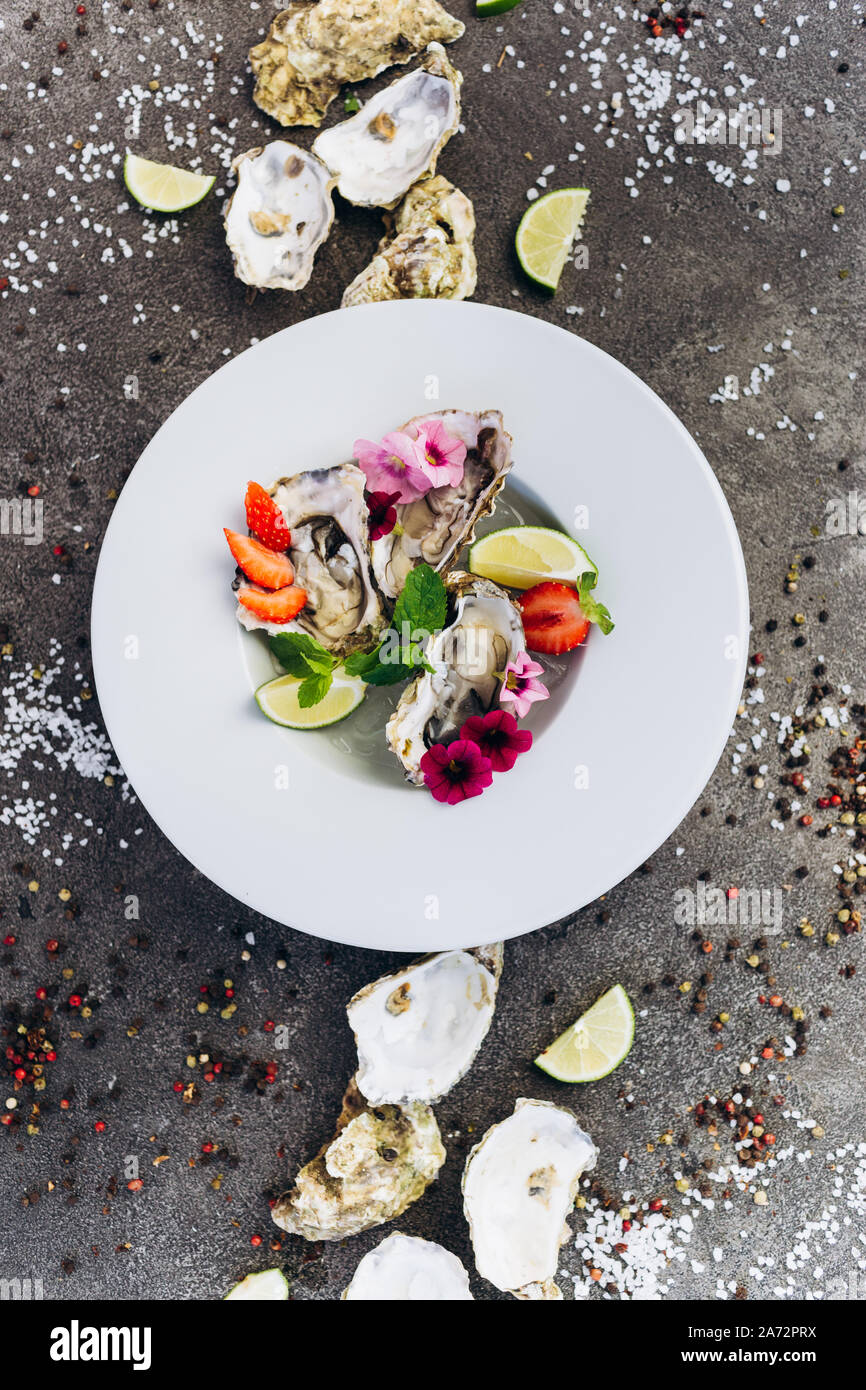 Las ostras en un plato decorado con flores sobre un fondo gris. Fotografía de stock -
