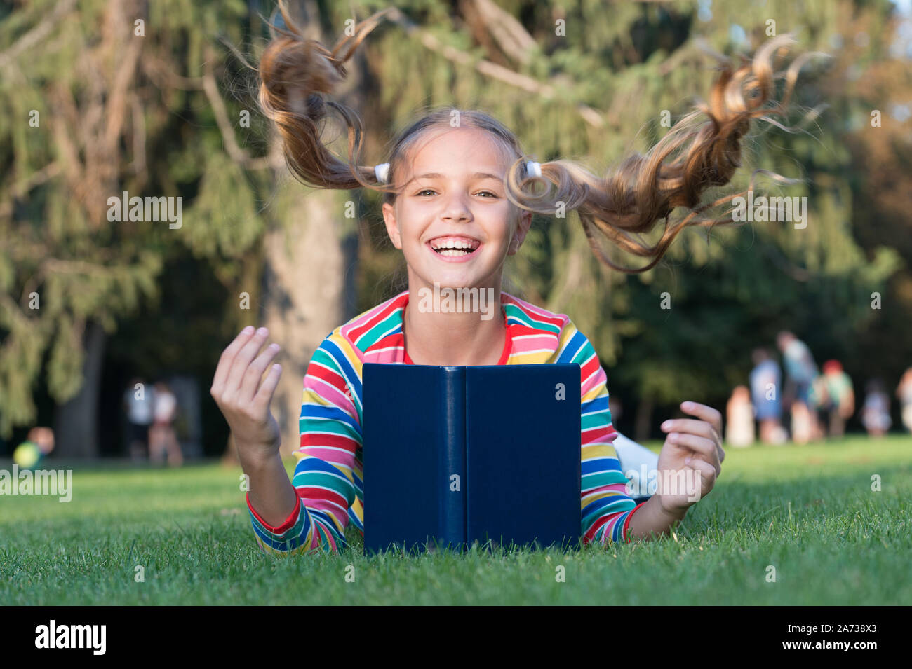 Obteniendo tu peinado volar. Niño feliz con el Flying peinado sobre la  hierba verde. Pequeña niña linda sonrisa con largas colas de peinado. La  moda look de peinado fácil. Conocimiento del libro.