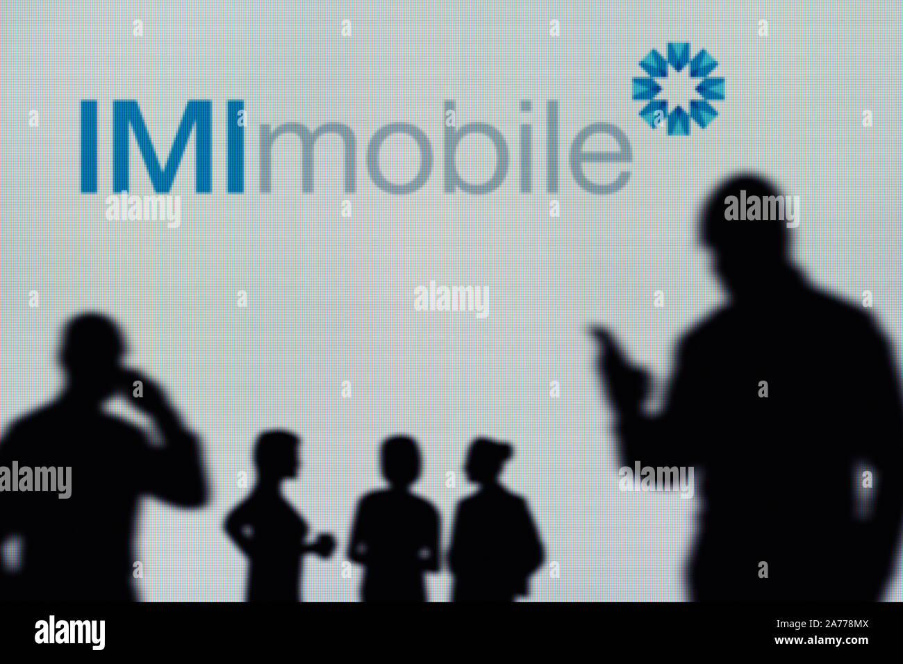 El logotipo de IMImobile es visto en una pantalla LED en el fondo mientras una silueta persona utiliza un smartphone (uso Editorial solamente) Foto de stock