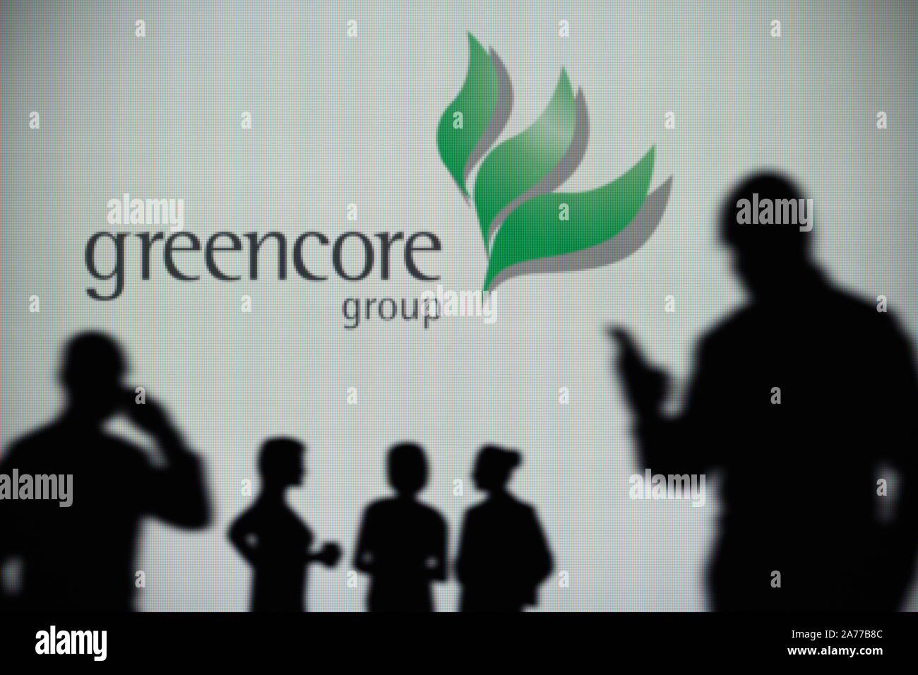 El Greencore logo es visto en una pantalla LED en el fondo mientras una silueta persona utiliza un smartphone (uso Editorial solamente) Foto de stock