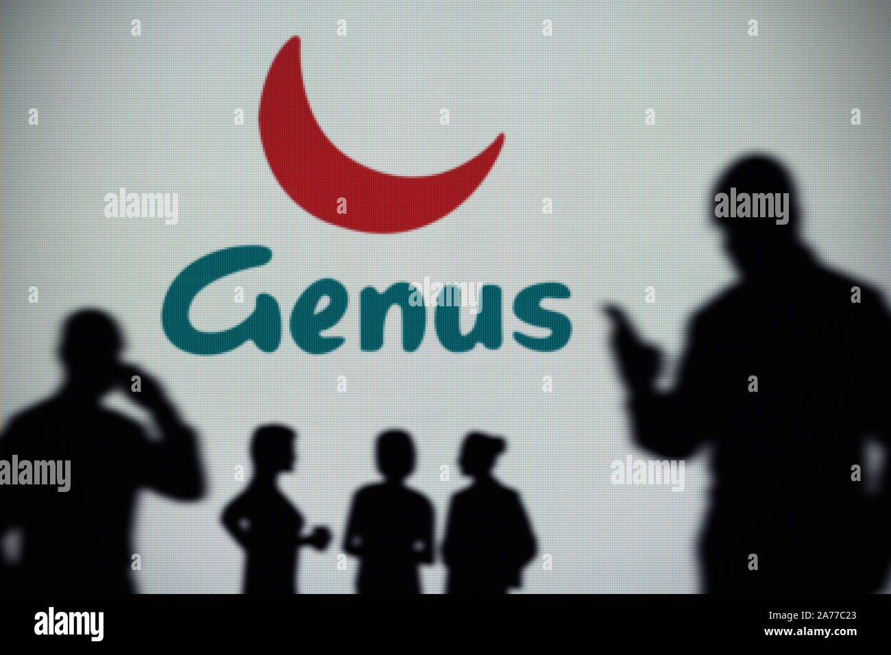 El Genus plc logo es visto en una pantalla LED en el fondo mientras una silueta persona utiliza un smartphone (uso Editorial solamente) Foto de stock