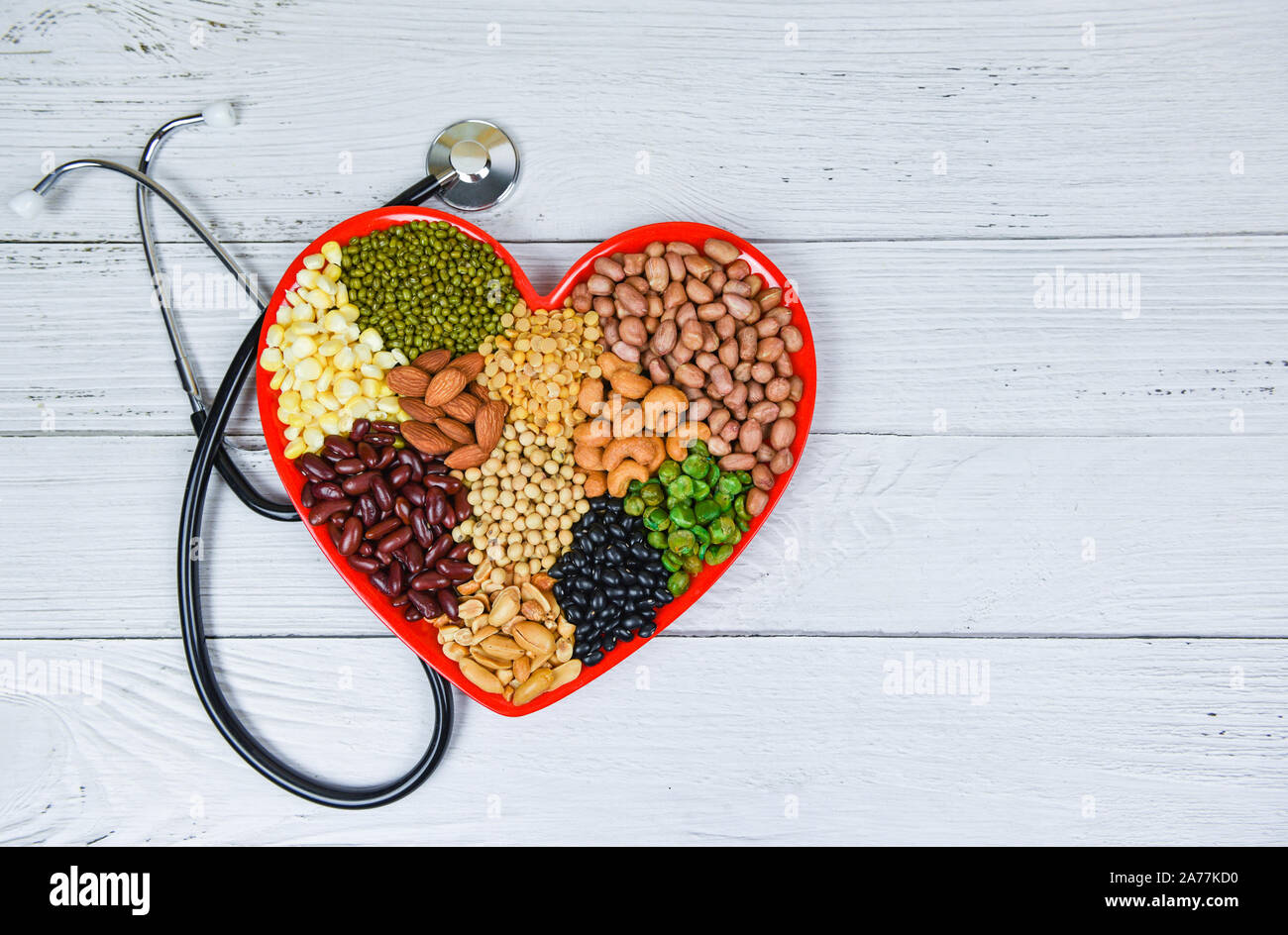 Selección de alimentos saludables para el corazón comer limpio vida colesterol concepto de salud / mixto diferentes frijoles nueces granos en la placa del corazón rojo para una sana foo Foto de stock