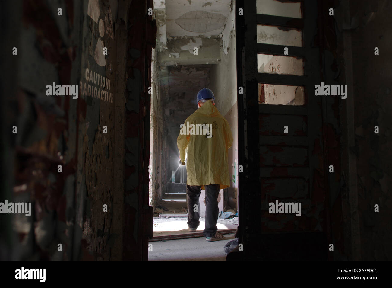 Un hombre en casco caminando en ruinas radiactivas. Un investigador con una linterna en un largo pasillo en el edificio destruido y olvidado. Símbolo nuclear con Foto de stock