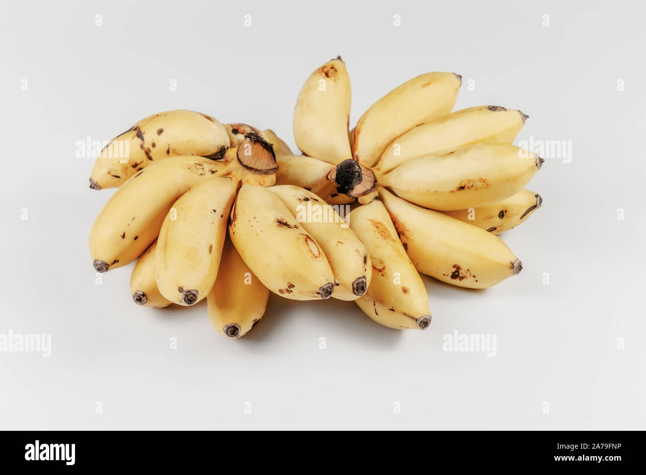 Pequeños plátanos maduros en racimos Caribe dama dedos exóticos fondo blanco amarillo Foto de stock