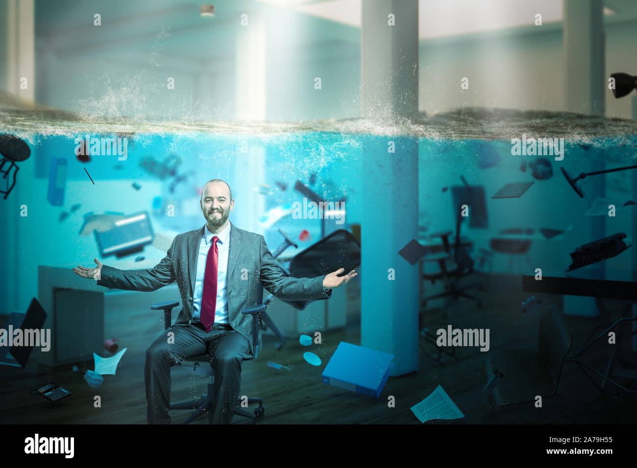 Empresario sonriente sentado en una oficina completamente inundados con objetos que flotan en el agua. Concepto de problemas en el trabajo y una visión positiva. Foto de stock