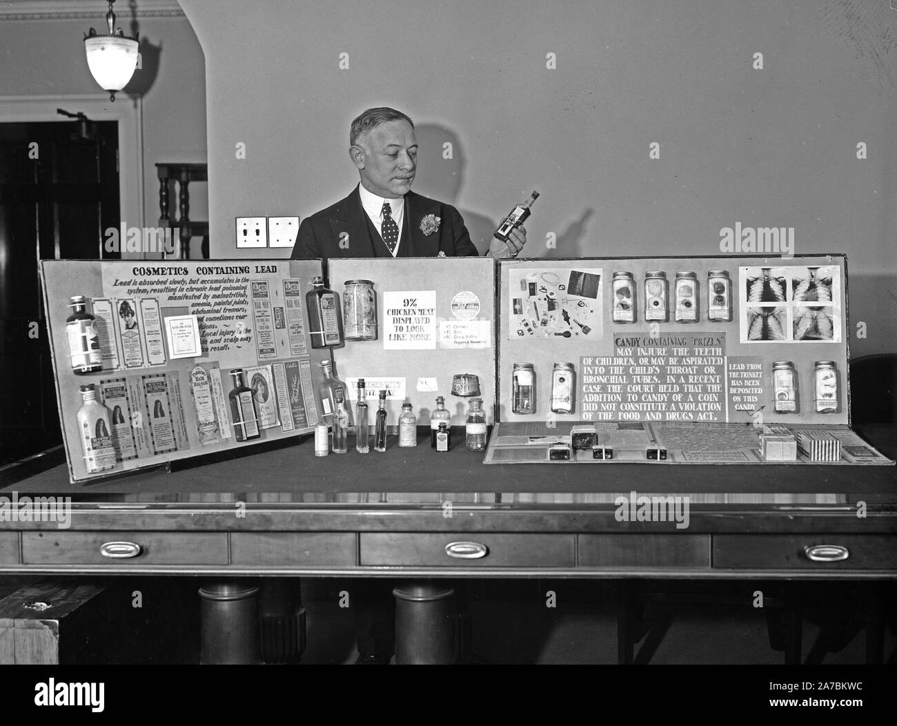Hombre de pie detrás de la pantalla mostrando diversos productos cosméticos que contienen plomo ca. 1934 Foto de stock