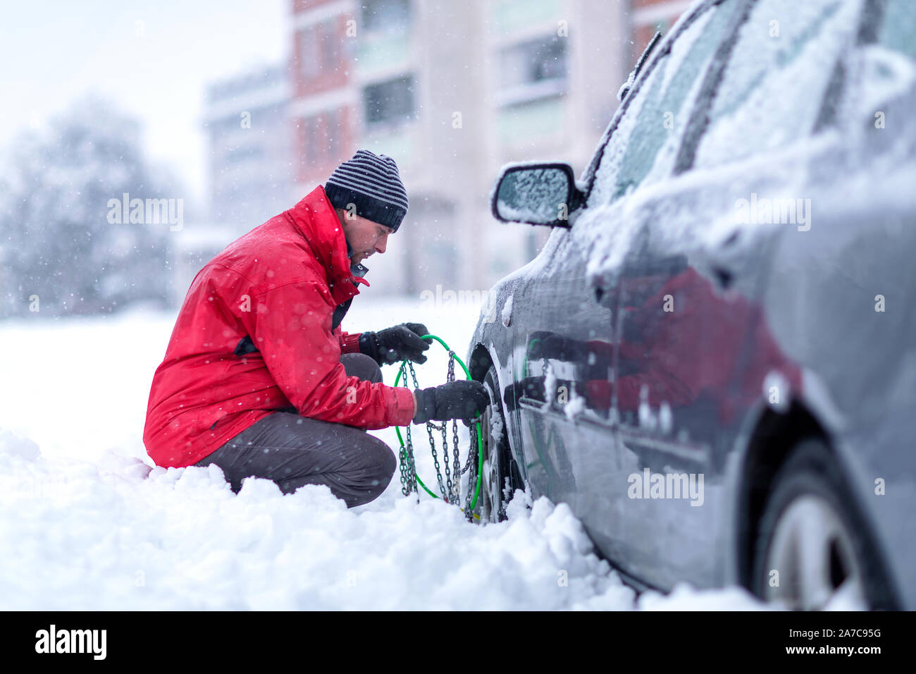 Joven poniendo cadenas de invierno en coche.confundido el hombre no sabe cómo poner las cadenas de nieve sobre los neumáticos de coche. Foto de stock