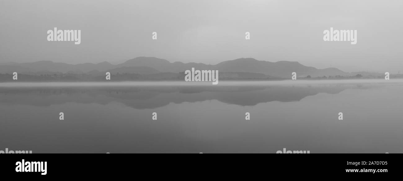 Reflejo de mountanis monocromos en un lago brumoso Foto de stock