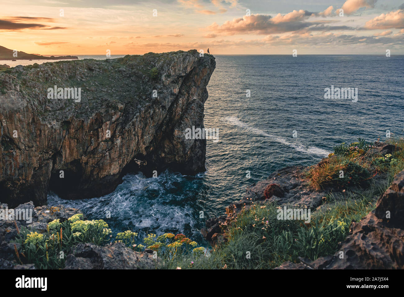Paisaje con la silueta de un hombre parado en el borde del acantilado en la costa del mar en el norte de España, Asturias, Europa en colorido atardecer en verano Foto de stock