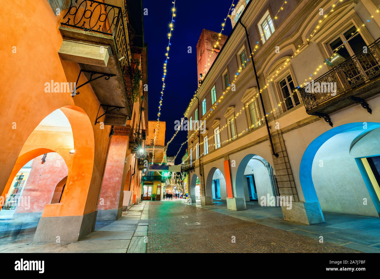 Calle peatonal adoquinada iluminada de noche con las luces de Navidad en el casco antiguo de la ciudad de Alba, Piamonte, Norte de Italia. Foto de stock