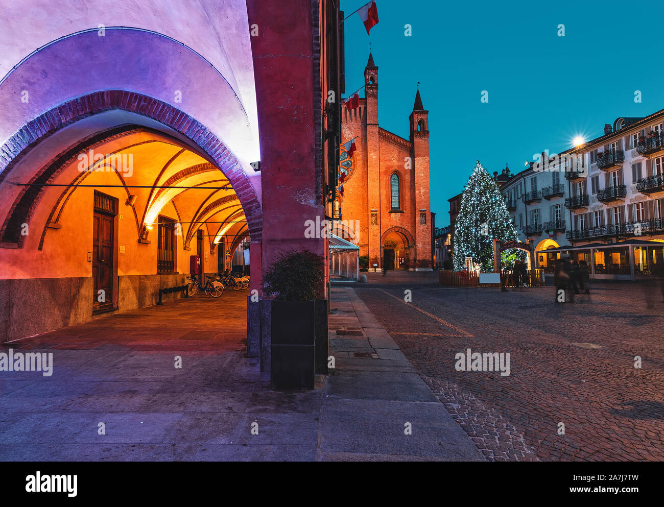 Vista de edificios iluminados y árbol de Navidad en la plaza de la ciudad de adoquines en la tarde en la pequeña ciudad de Alba, Piamonte, Norte de Italia. Foto de stock