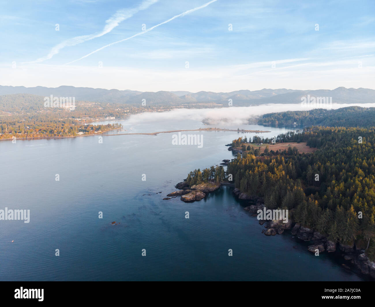 Vista aérea de un banco de niebla mar moviéndose hacia abajo en una bahía sobre un la escarpada costa de la isla de Vancouver. Foto de stock