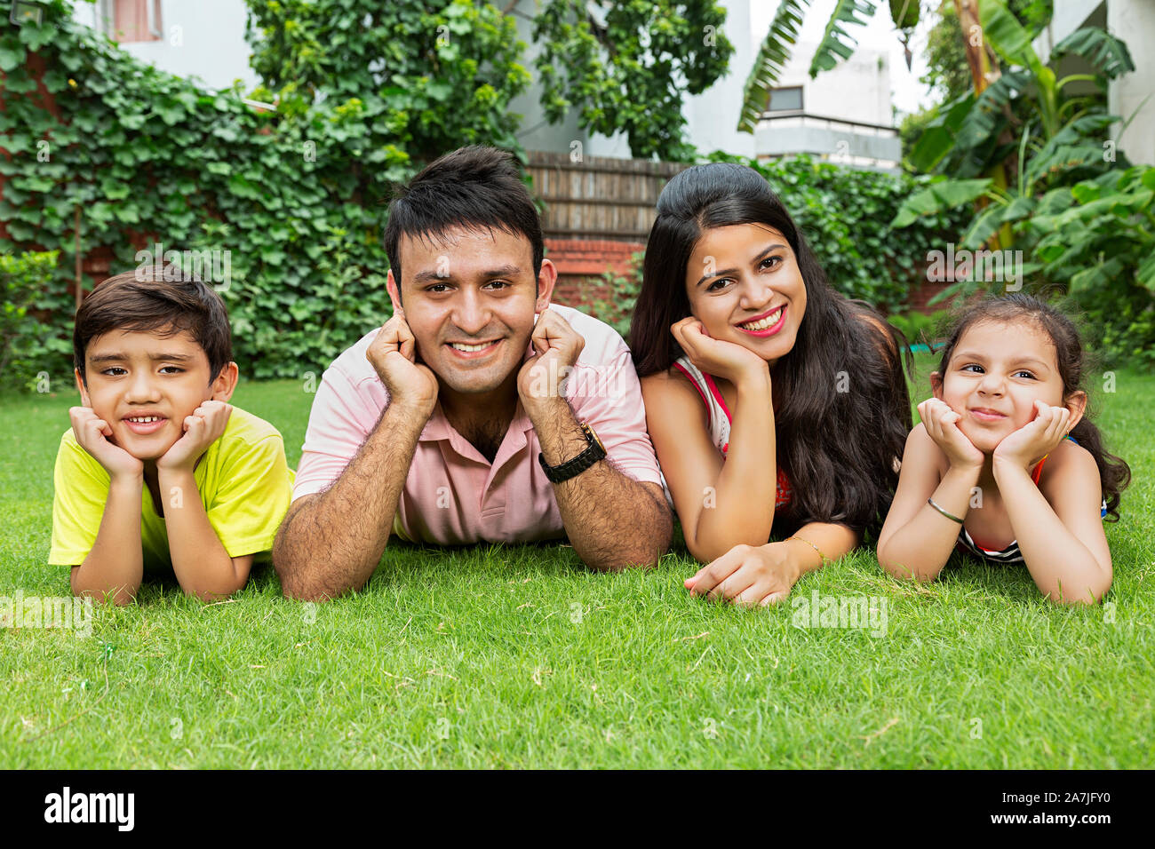 Los padres de familia feliz y relajada Two-Children acostado sobre la hierba juntos en el jardín de su casa Foto de stock