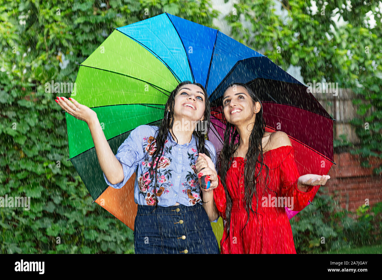 Feliz dos amigas jóvenes bajo paraguas disfrutando en la lluvia en la  piscina en el jardín Fotografía de stock - Alamy