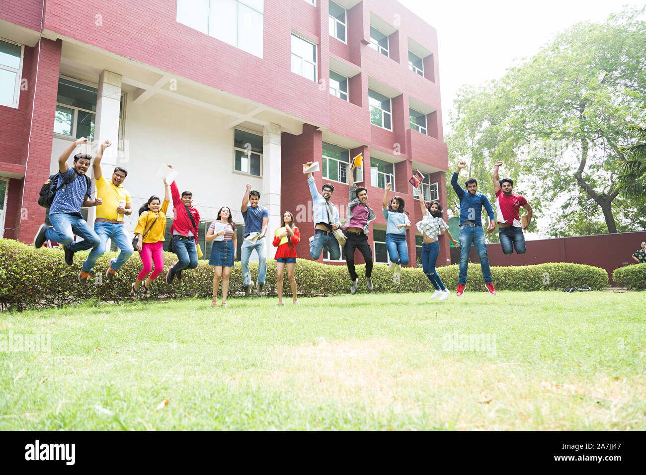 Grupo de jóvenes varones y mujeres estudiantes universitarios amigos saltando arriba Mid-Air In-Outside Edificio del campus Foto de stock