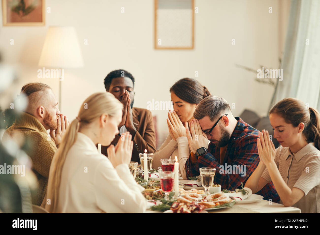 Grupo multiétnico de gente diciendo la gracia en mesa durante la Navidad banquete con amigos y familia Foto de stock