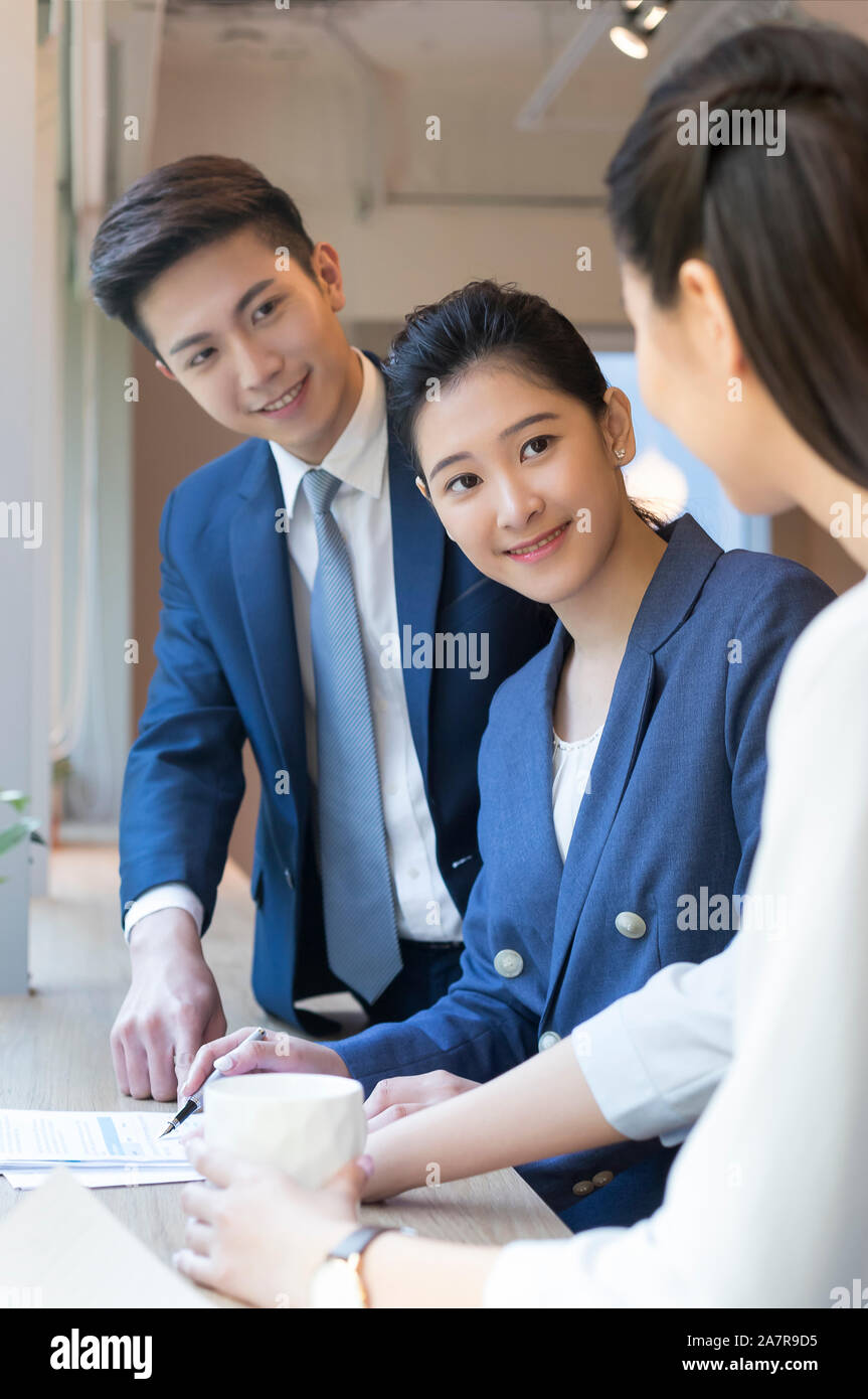 Grupo de ti jóvenes empresarios sonrientes hablando en un escritorio en una oficina mientras trabajan juntos Foto de stock