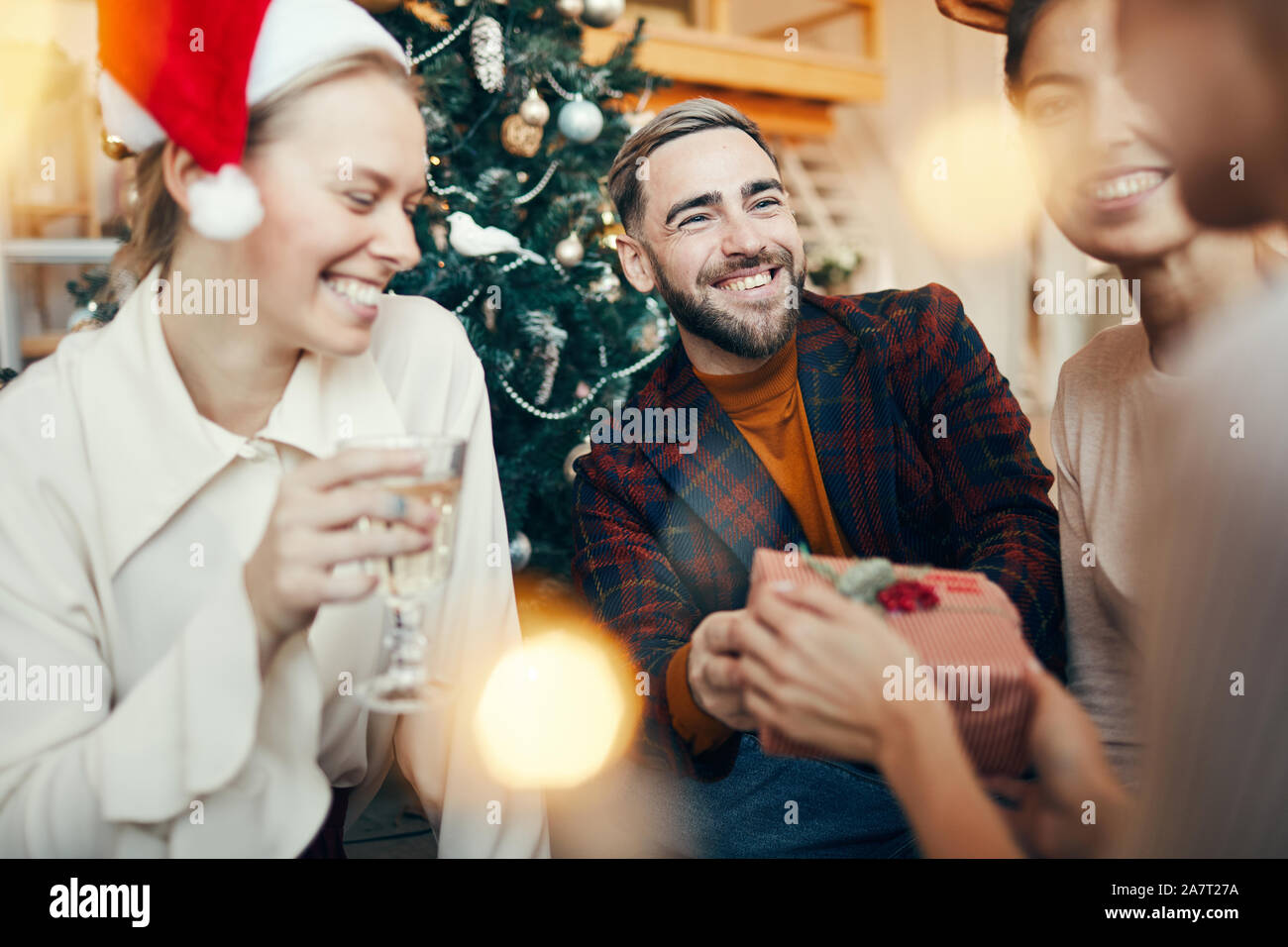 Retrato de un hombre adulto elegante sonriendo felizmente mientras intercambian regalos con los amigos durante la fiesta de Navidad Foto de stock