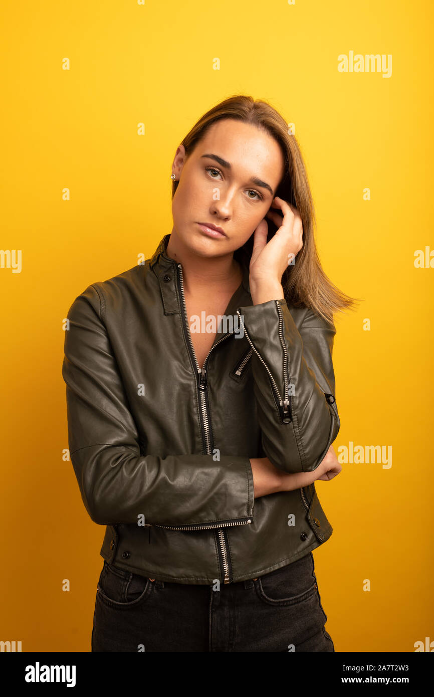 Retrato de una joven mujer vistiendo una chaqueta de cuero en la parte delantera del fondo amarillo Foto de stock