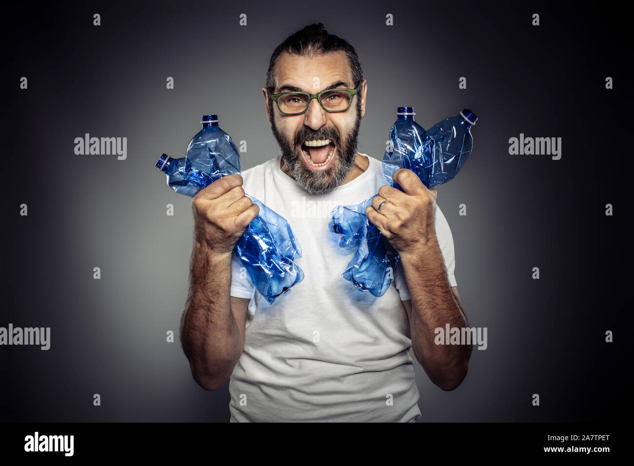 Retrato de estudio de un hombre con barba y gafas que está sosteniendo botellas vacías de plástico en sus manos. Concepto de reciclaje y uso excesivo de plástico Foto de stock