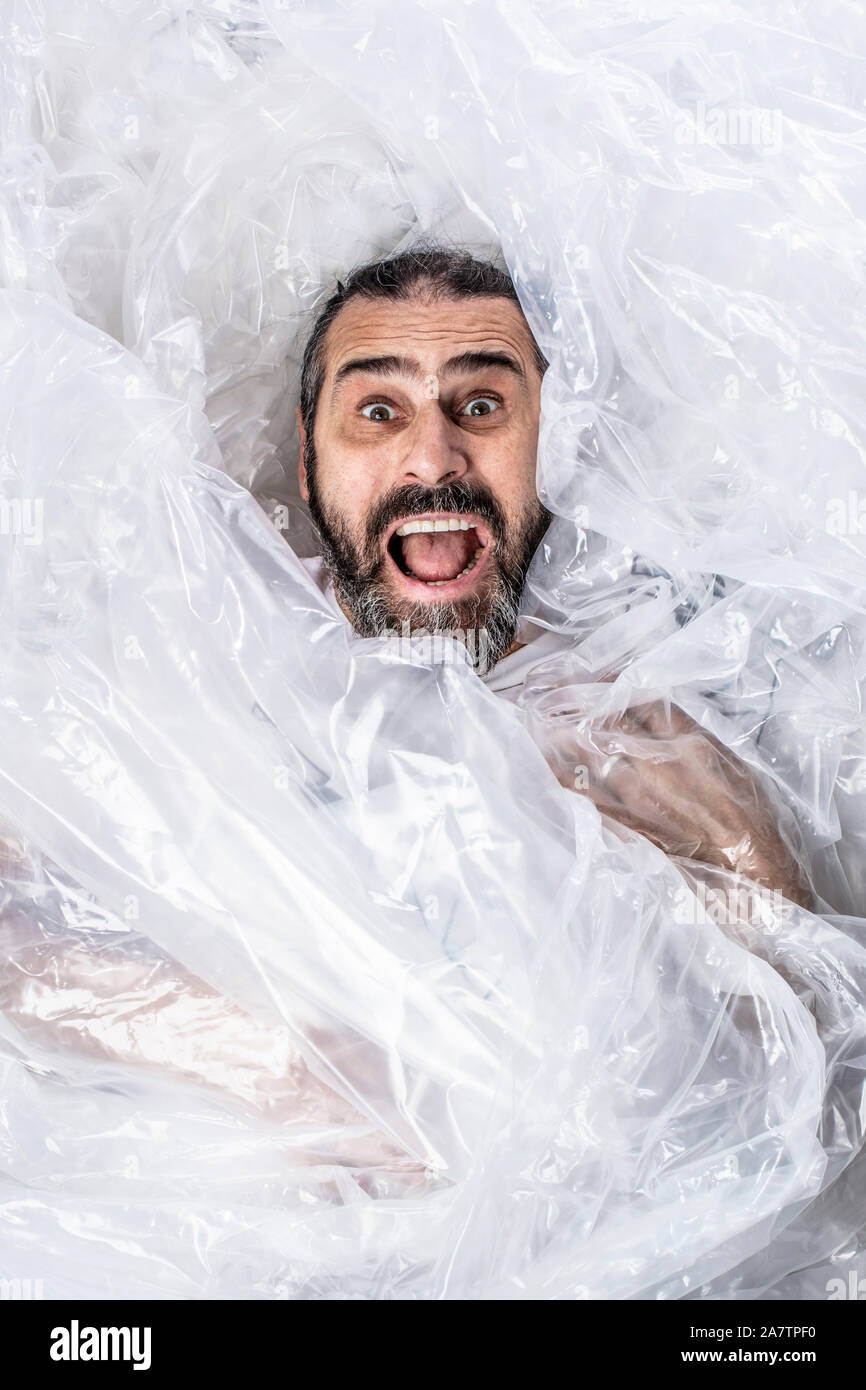 Retrato de un hombre barbado envuelto en plástico enrollado. sorprendida expresión e intención de gritar. Foto de stock