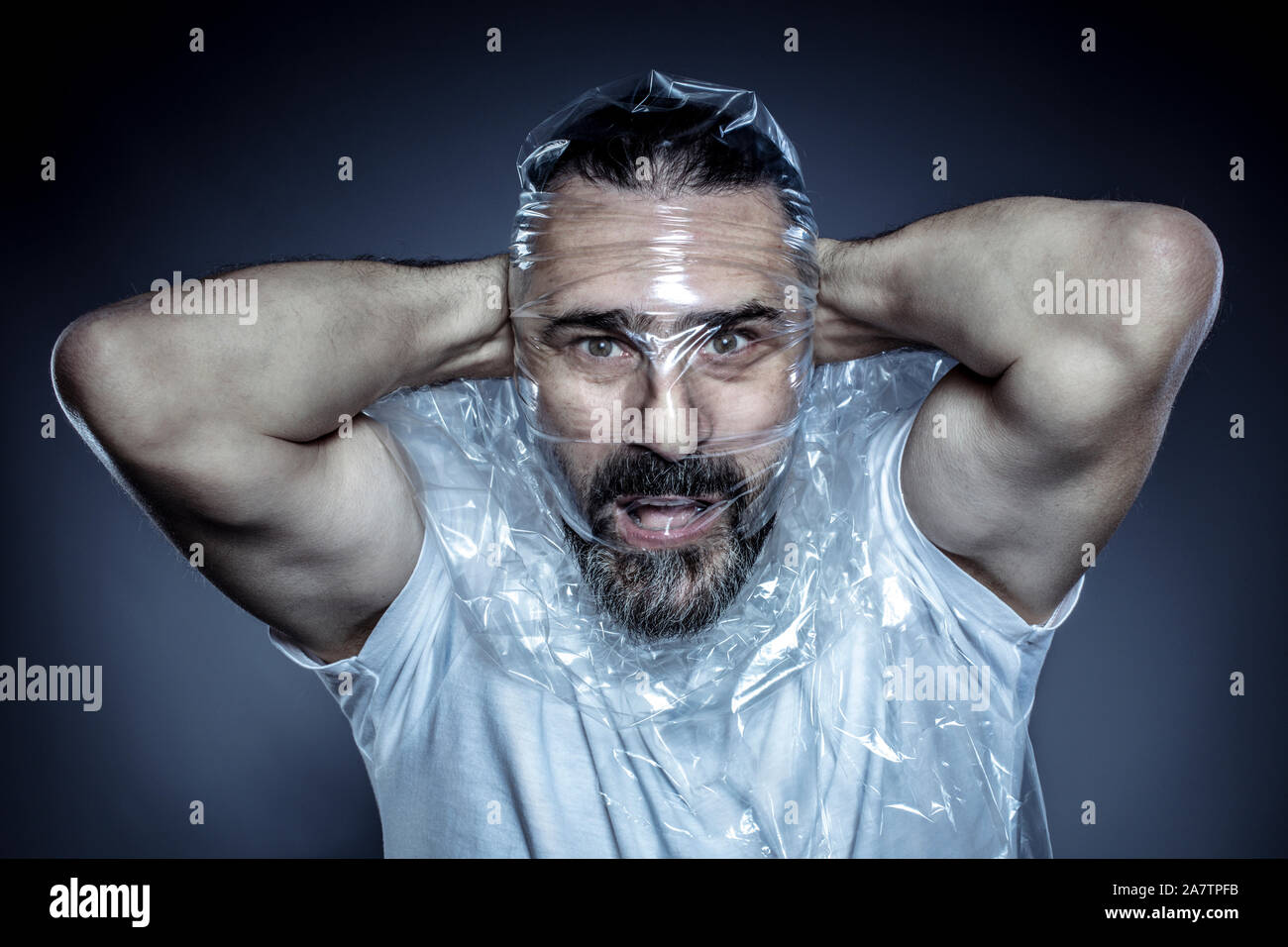 Retrato de un hombre con barba y su rostro envuelto en una película de plástico. Concepto de toxicidad de los materiales plásticos y su uso excesivo en la vida común Foto de stock